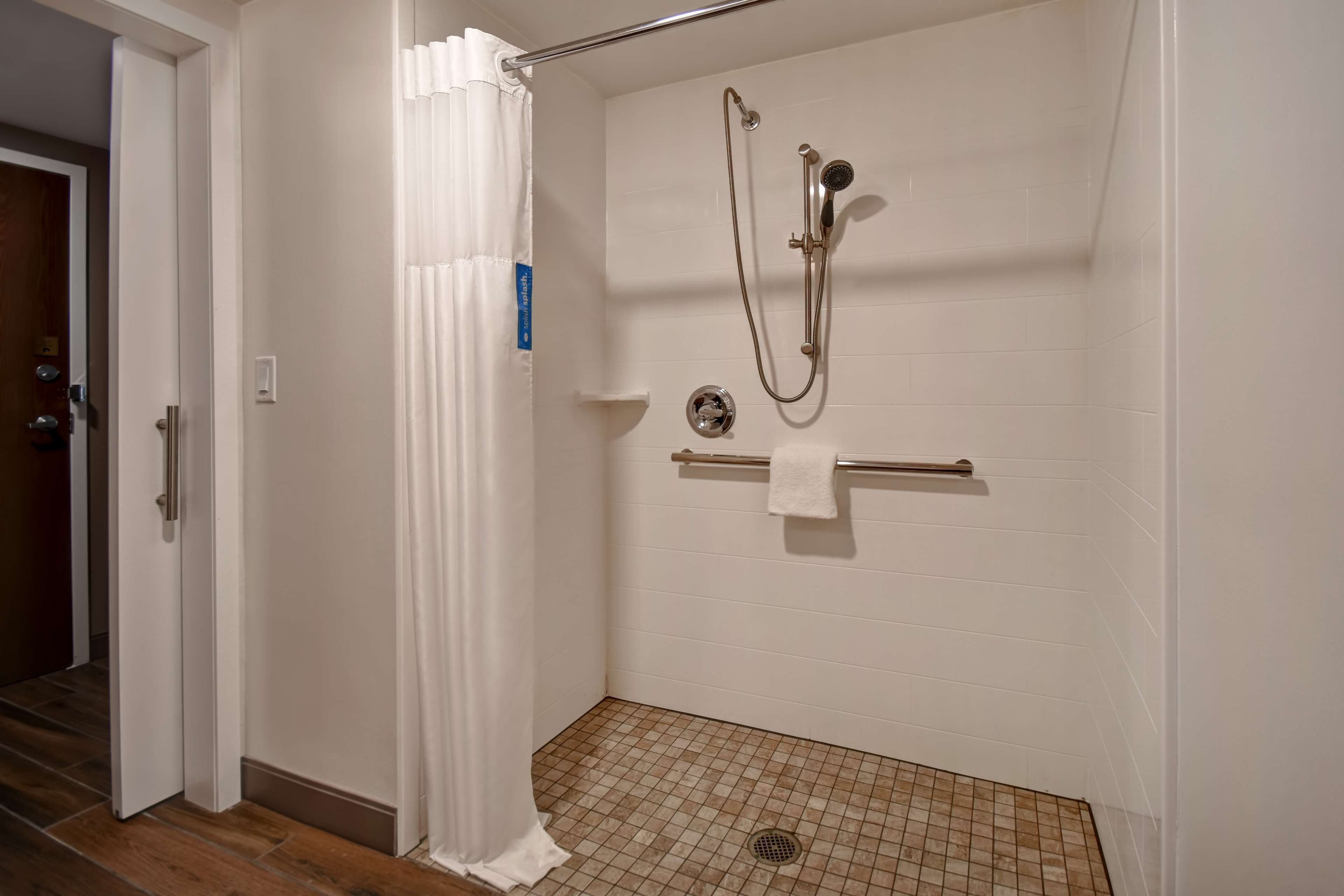 A shower with a handheld showerhead, a towel rack, and a drain.