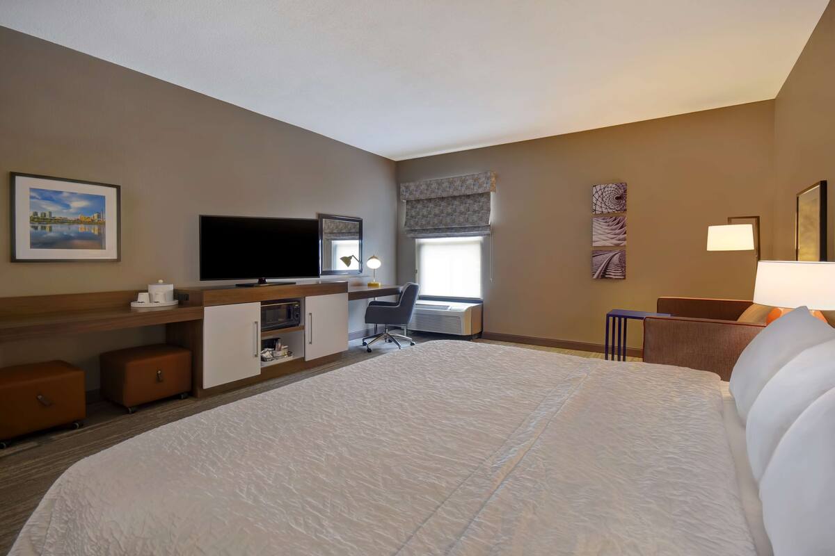 A hotel room with a large bed, a desk with a computer, a television, and a window with a view.