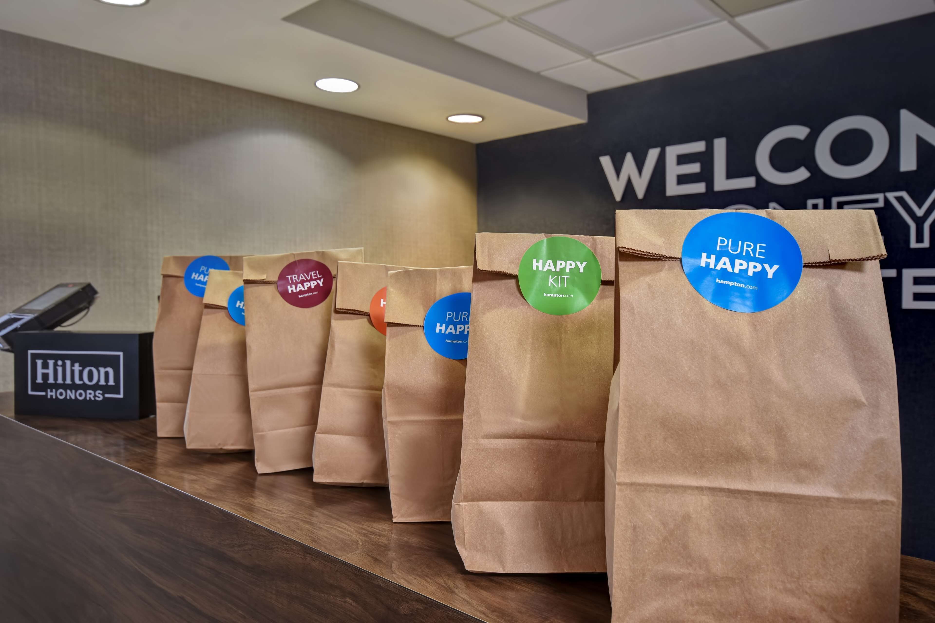 A row of brown paper bags with stickers labeled "PURE HAPPY" and "HAPPY KIT" on a counter in a hotel lobby.