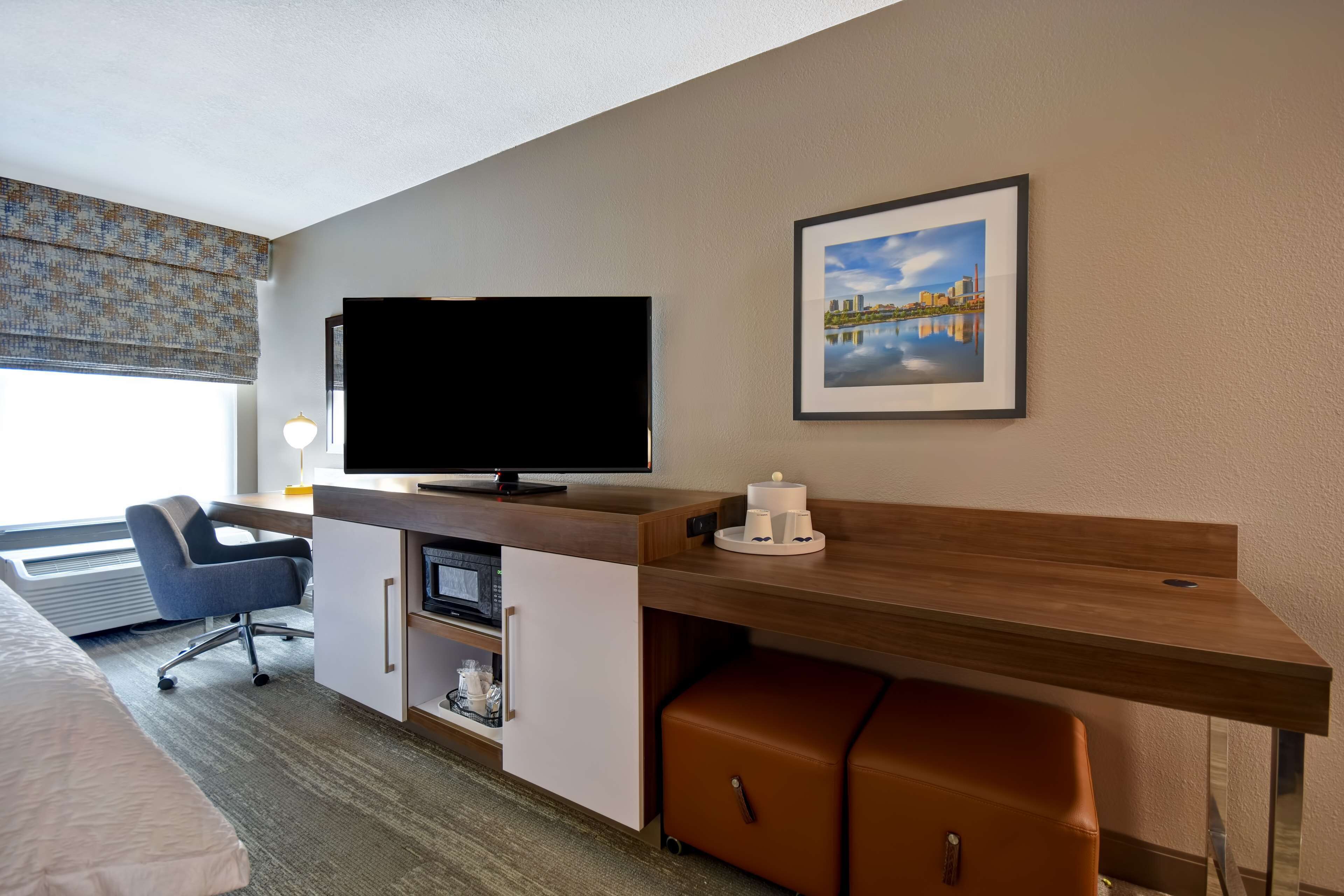 Habitación de hotel con cama, escritorio, televisor de pantalla plana, una silla, microondas y un mueble pequeño.