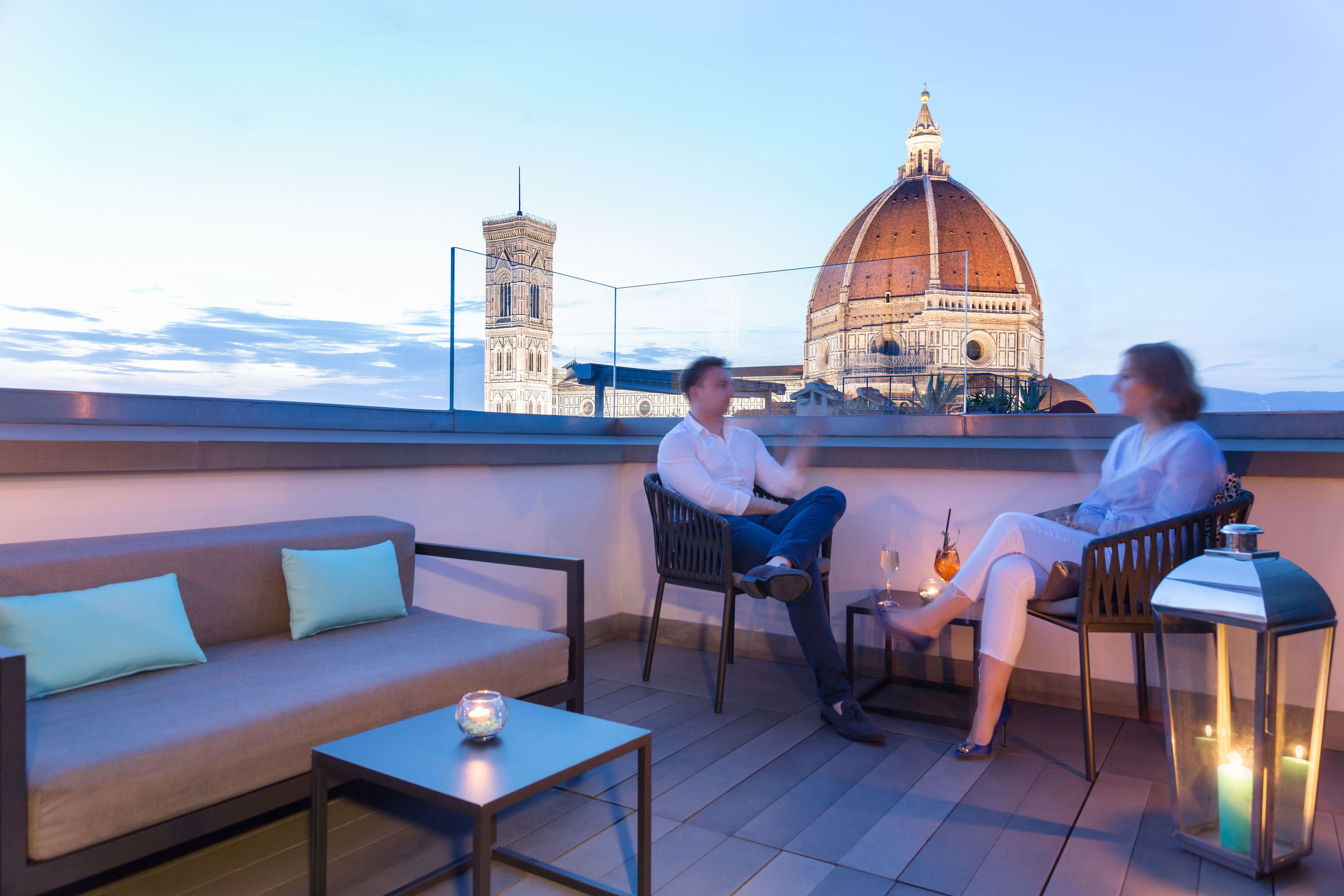 A rooftop terrace with a sofa, chairs, and a table. A large domed building and a tower are visible in the background.