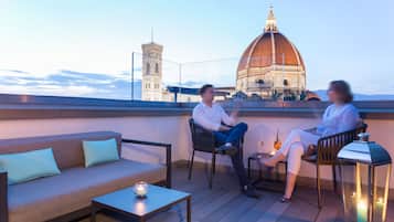 A rooftop terrace with a sofa, chairs, and a table. A large domed building and a tower are visible in the background.