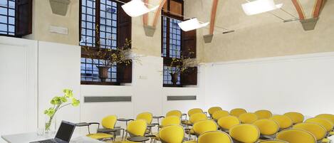 A conference room with yellow chairs, a white table with a laptop, and large windows with decorative plants.