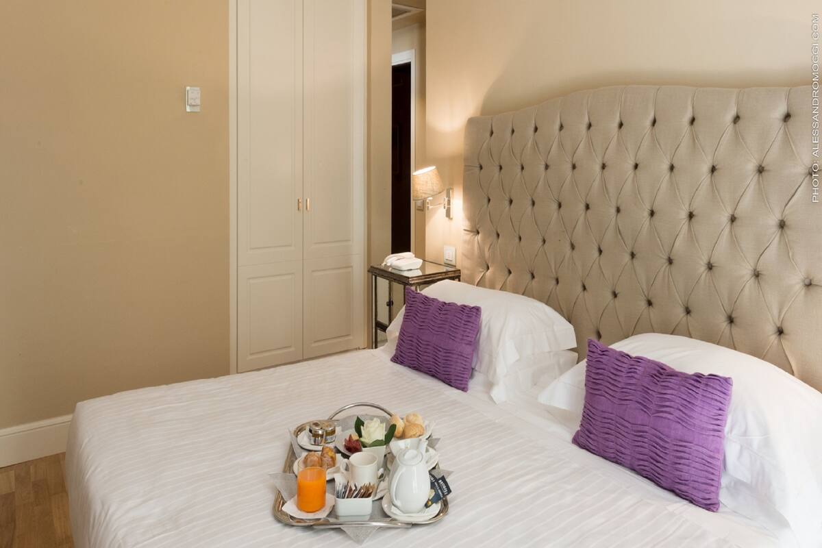 Une chambre d’hôtel avec un grand lit, une table de chevet, un plateau avec des articles pour le petit-déjeuner et une armoire.