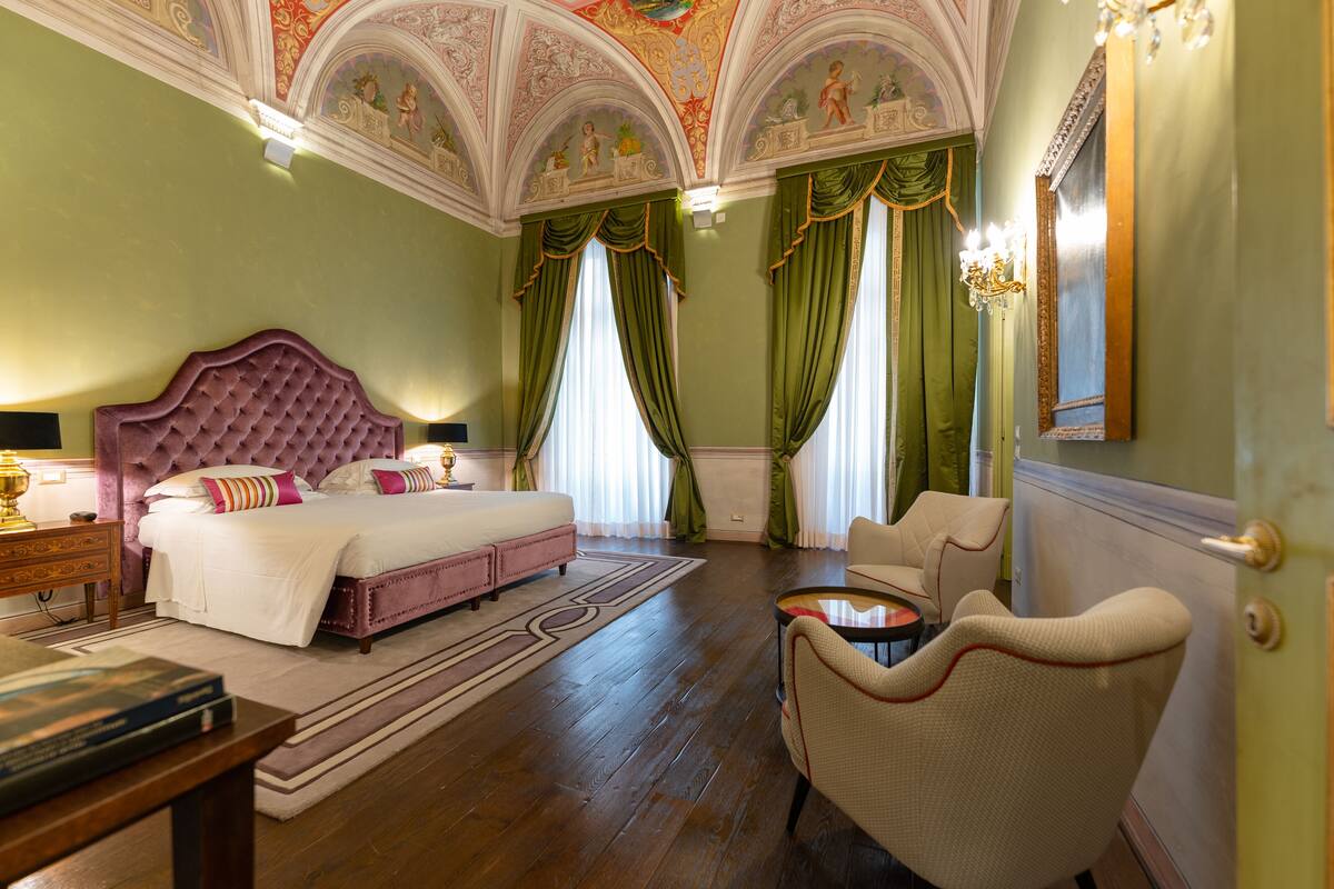 Une chambre spacieuse avec un grand lit, un coin salon et un lustre.