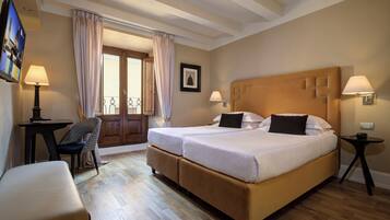 A hotel room with two beds, a desk, a chair, and a TV.