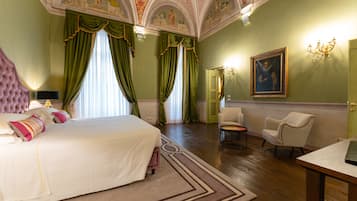 A spacious bedroom with a large bed, green curtains, a chandelier, and a painting on the wall.