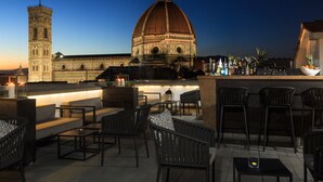 Un área con mesas y sillas para disfrutar al aire libre, un bar y vistas a un edificio histórico con cúpula y torre.