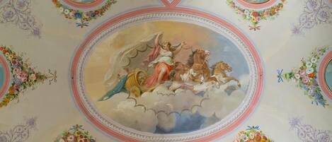 A ceiling with a central oval painting of a mythological scene, surrounded by floral decorations and smaller circular paintings.