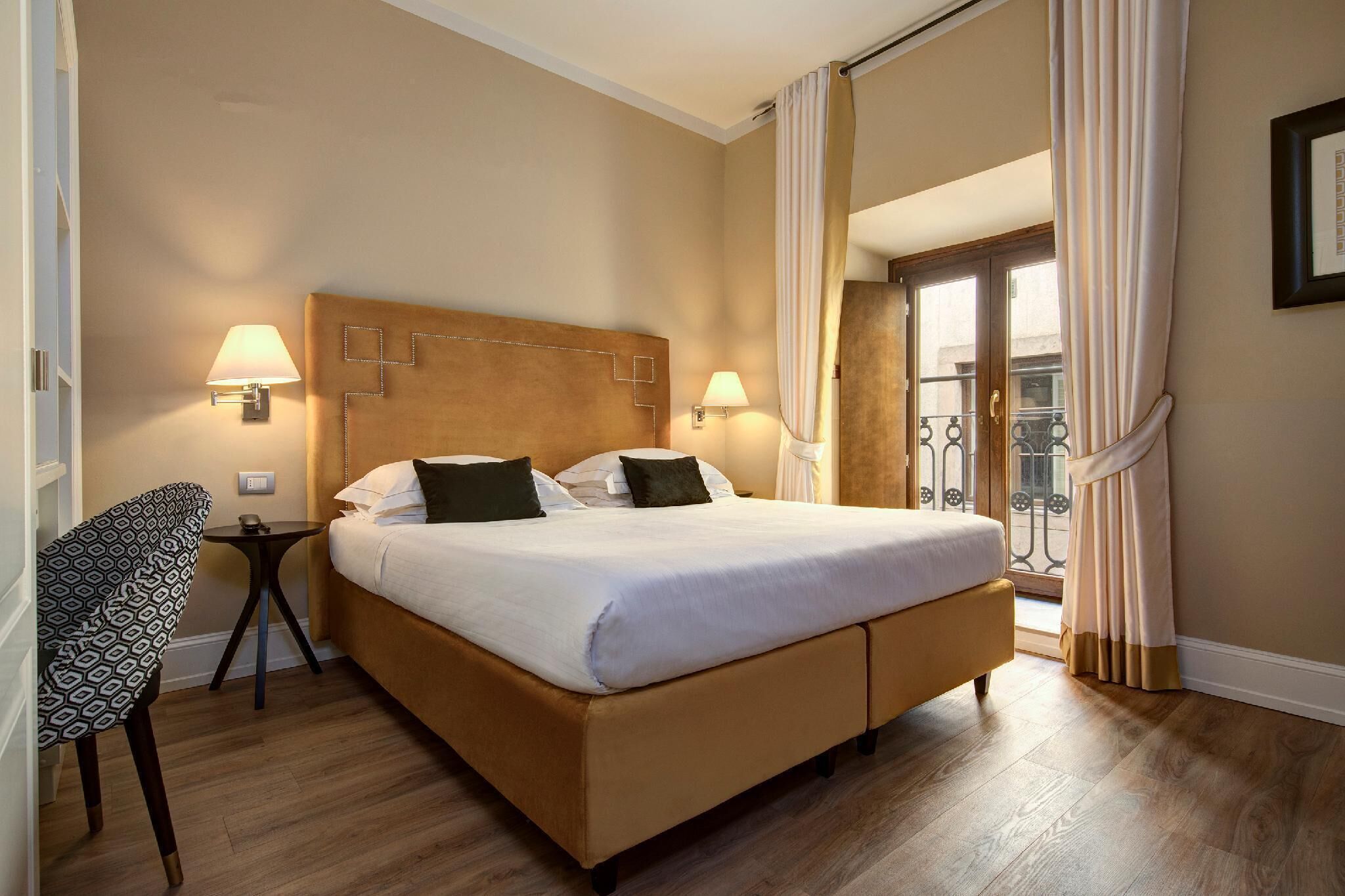 Una habitación de hotel con una cama grande, dos lámparas de noche, una mesita y una silla.