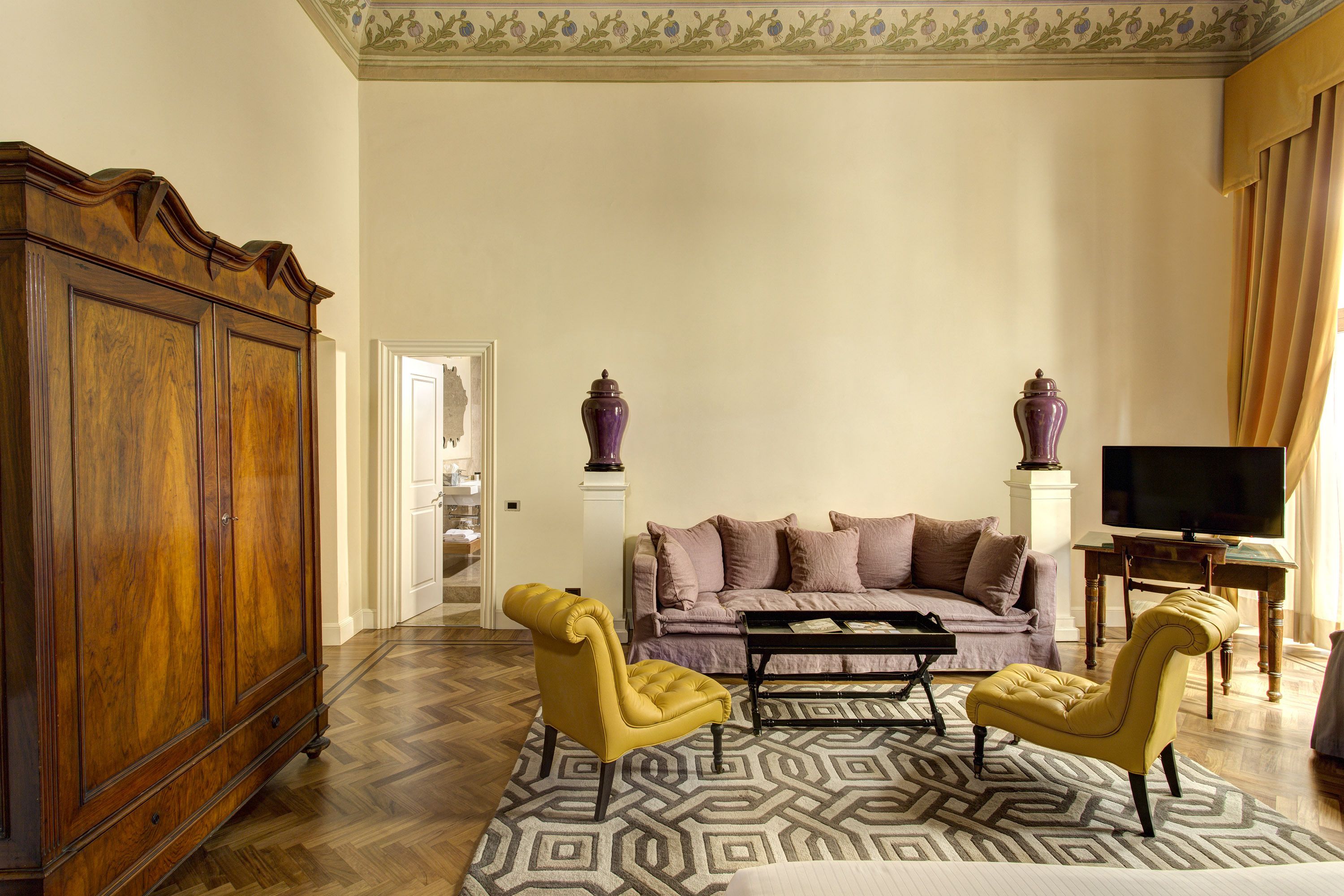 Una sala de estar con un mueble de madera grande, un sofá, dos sillones, un tapete estampado y una televisión.