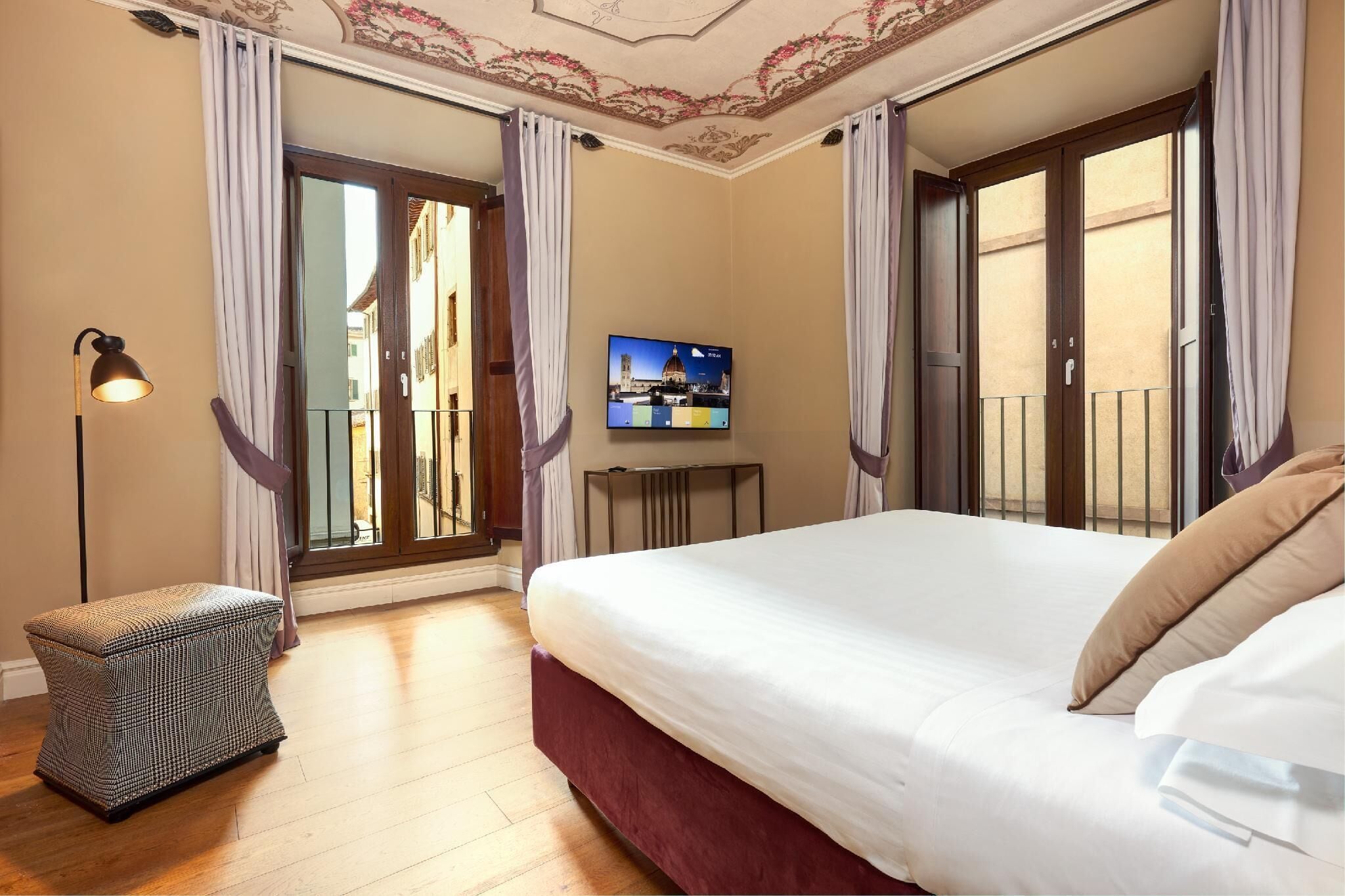 A bedroom with a large bed, a small table, a TV, and a balcony with curtains.