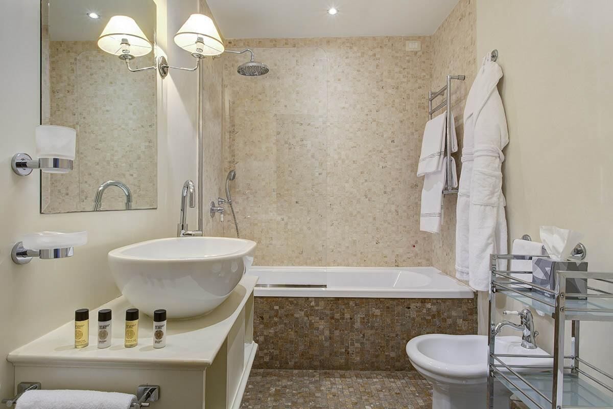 A modern bathroom with a large sink, bathtub, and bidet. There are toiletries on the counter and a towel rack with towels.