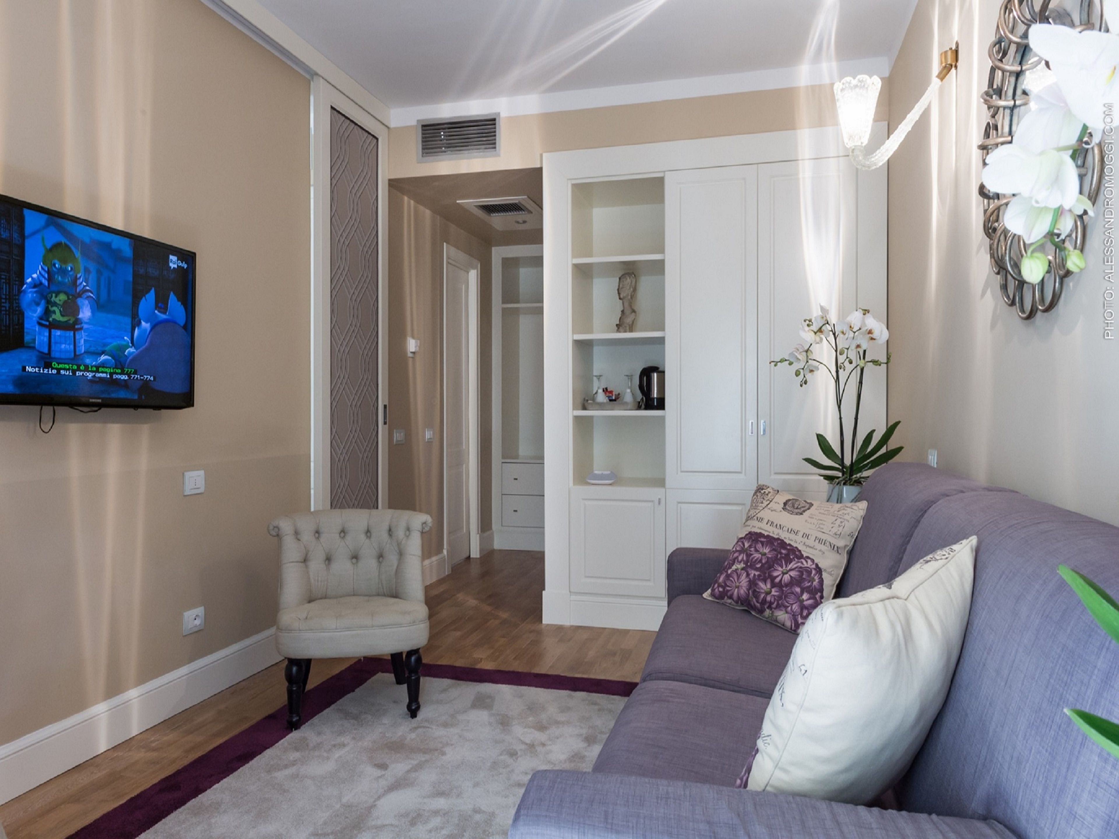 Sala de estar com televisão, sofá, poltrona e planta decorativa.
