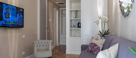 Sala de estar com televisão, sofá, poltrona e planta decorativa.