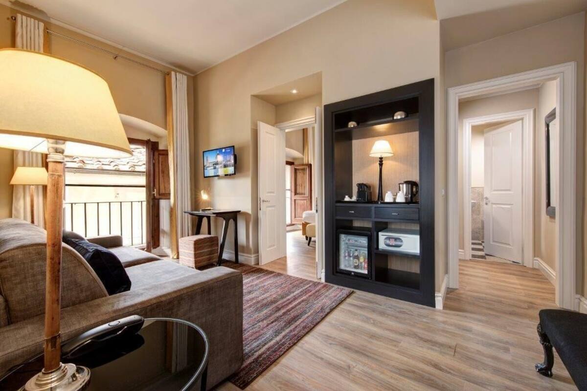 Une chambre d’hôtel équipée d’un canapé, d’une table basse, d’une lampe, d’un téléviseur, d’un mini-bar et d’une porte donnant sur une autre pièce.