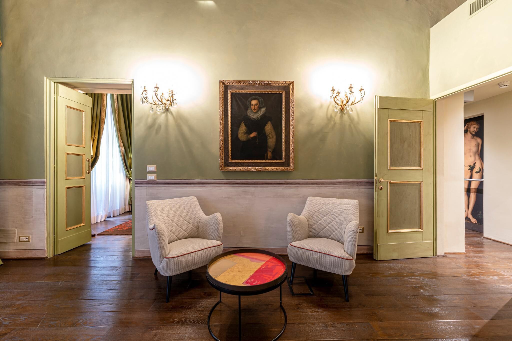 A room with two armchairs, a round table, a framed painting, and a door leading to another room.