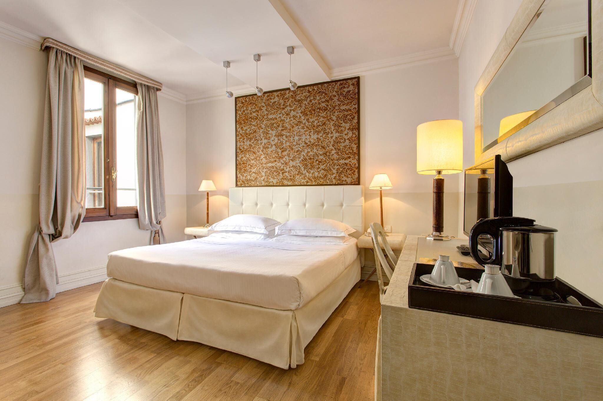 Habitación de hotel con una cama grande, dos lámparas de noche, cafetera y un espejo en la pared.