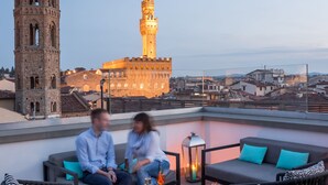 Una terraza en la azotea con zona de estar, una mesa con velas y vistas a una torre histórica y una fortaleza al fondo.