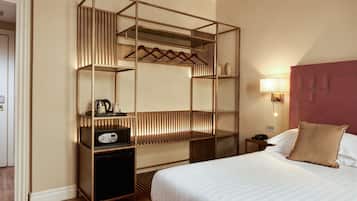 Habitación de hotel con cama, minibar, armario empotrado, mesita de noche y lámpara de pared.