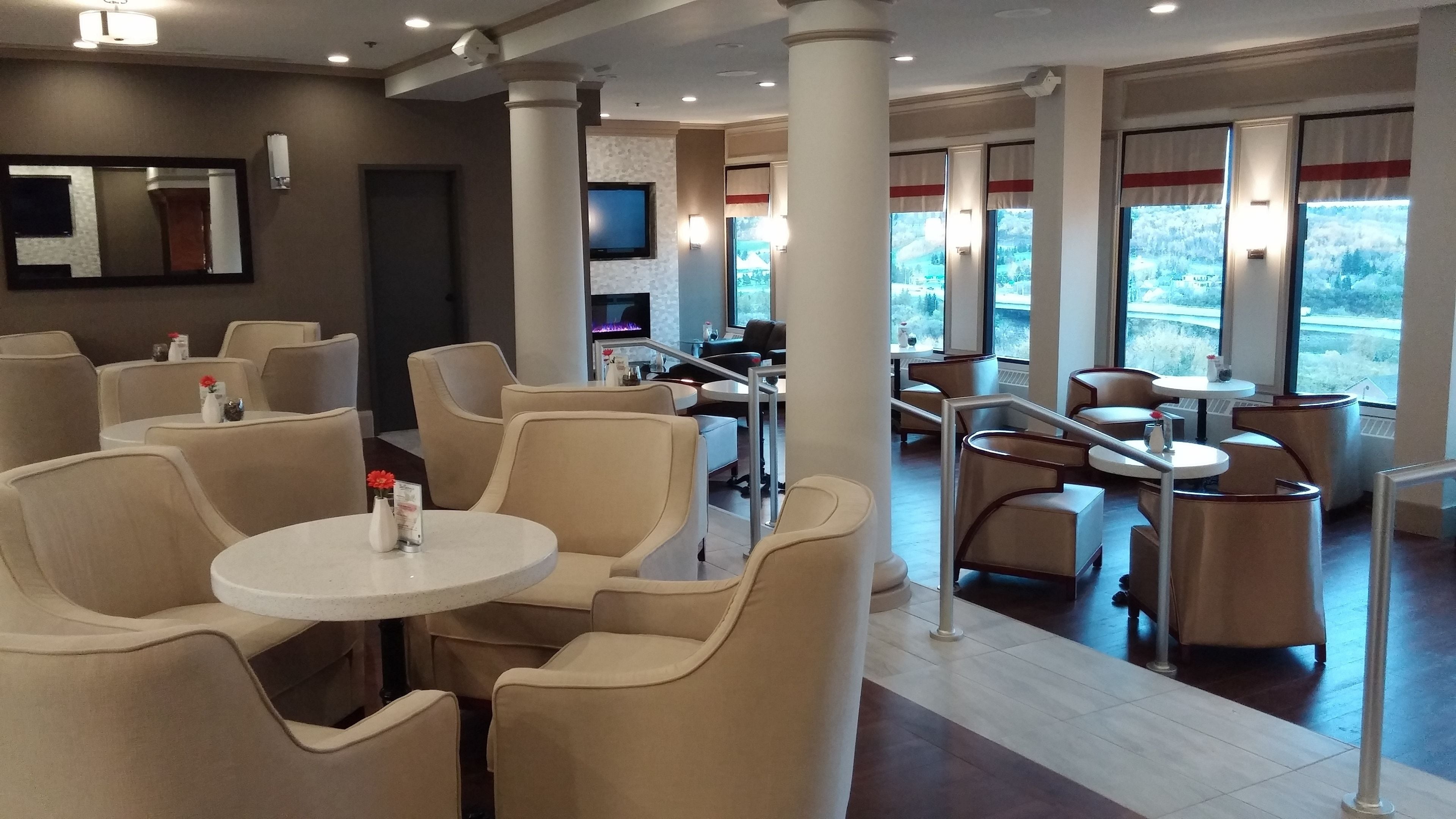 A hotel lobby with beige seating, a TV, and large windows with a view.