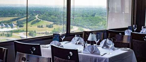 Un restaurante con una mesa dispuesta para dos, con vistas a un paisaje pintoresco con árboles y una carretera.
