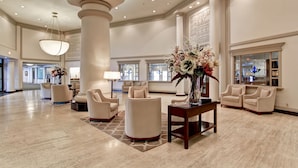 A spacious lobby with high ceilings, large columns, and a chandelier. There are several seating areas with armchairs and a coffee table. - Chateau Lacombe Hotel (Edmonton)