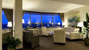 A hotel room with a city view, a sofa, a chair, a desk, and a lamp. - Chateau Lacombe Hotel (Edmonton)