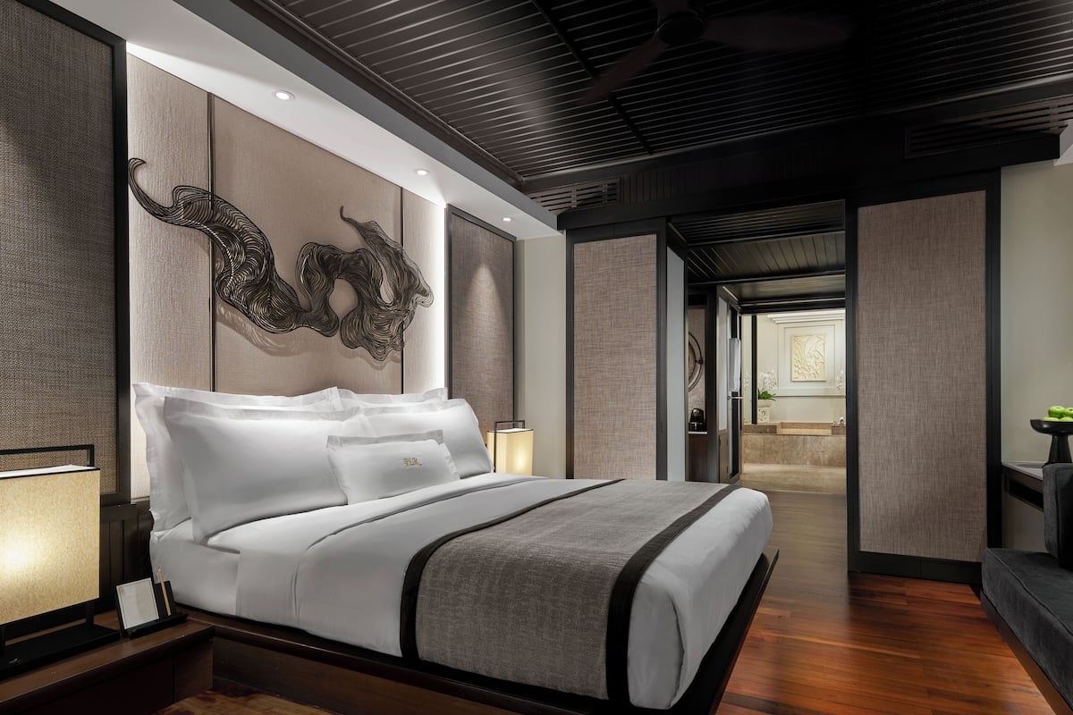 A modern hotel room with a large bed, a nightstand, a desk, and a view into the bathroom.