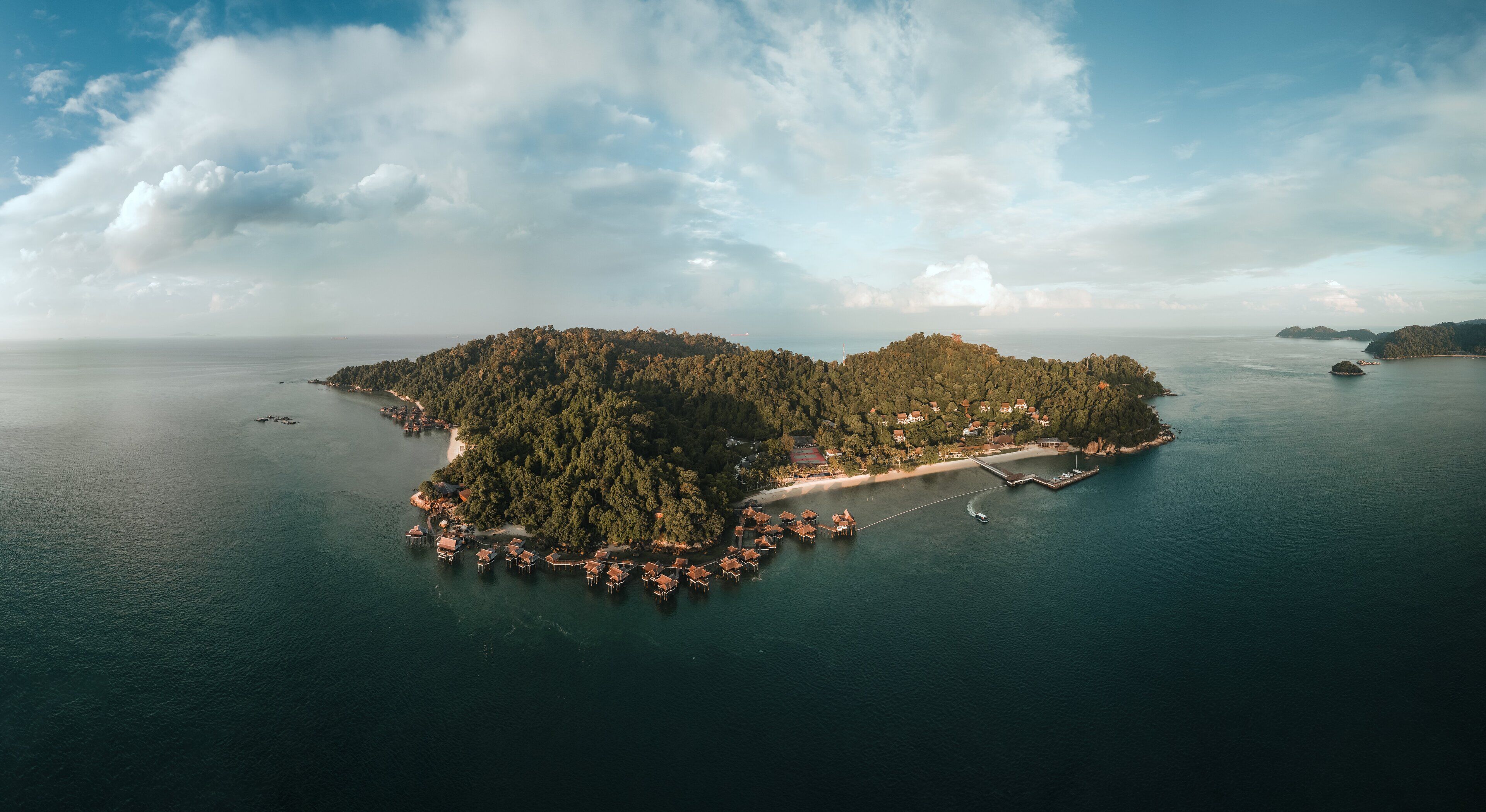 Vista aérea de una isla tropical con playa, bungalows sobre el agua y un muelle.