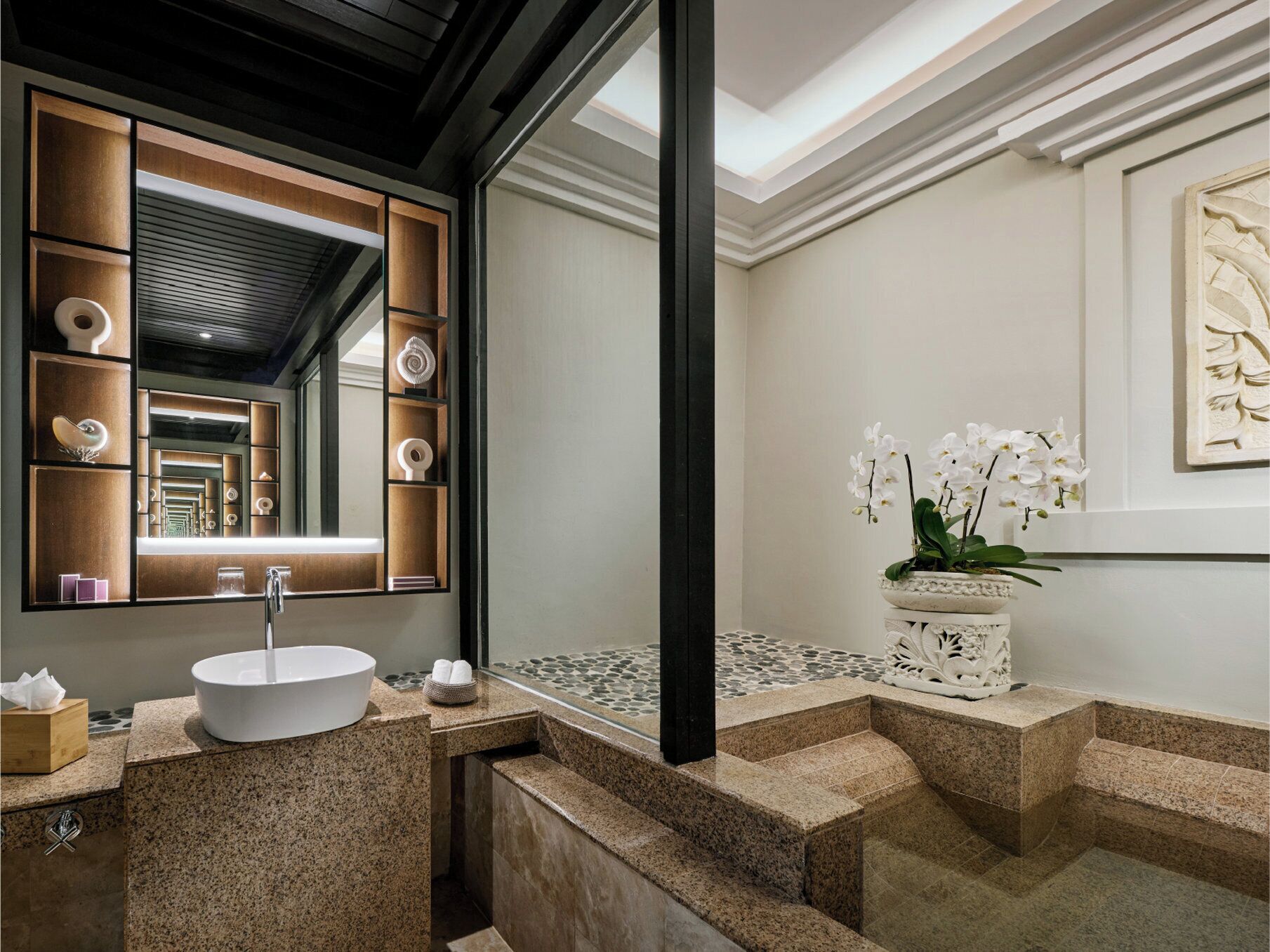 A modern bathroom with a large mirror, a white sink, and a decorative orchid plant.