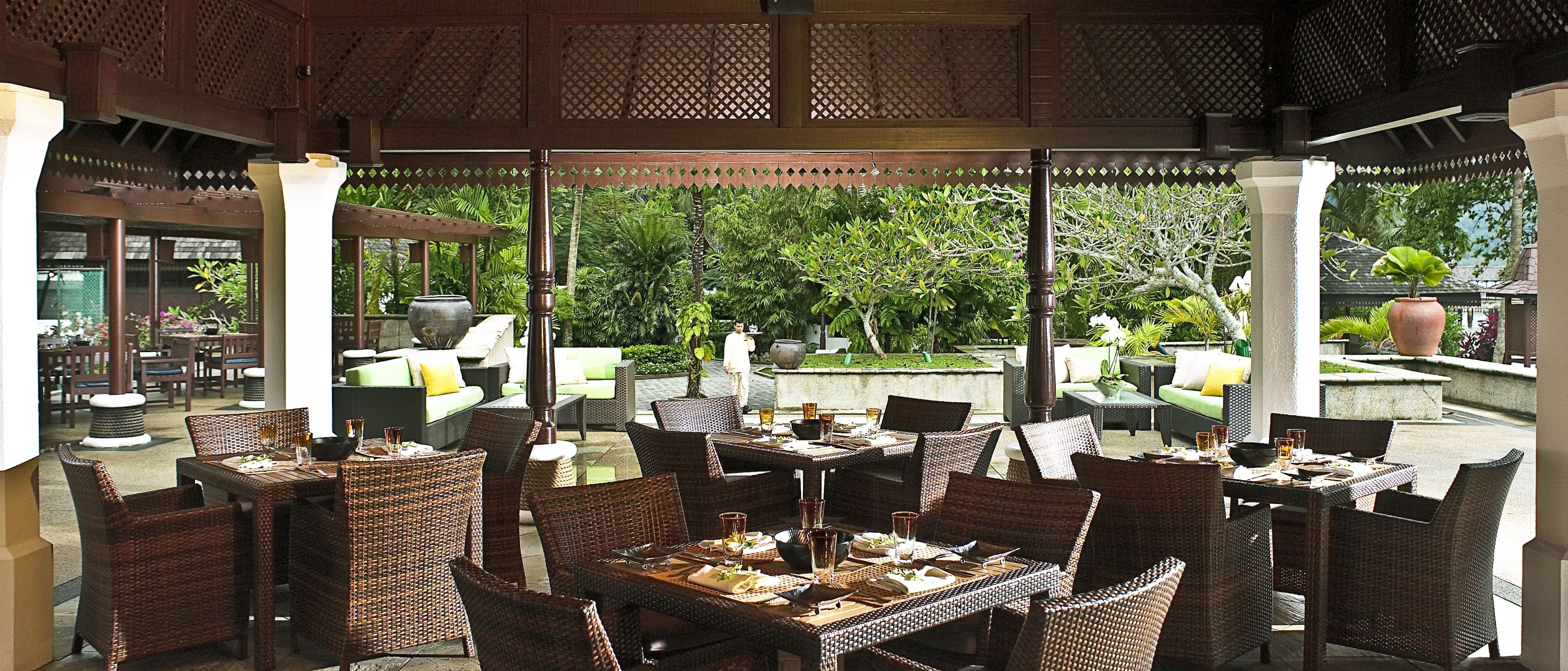 An outdoor dining area with wicker furniture and a view of lush greenery.