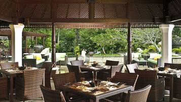 An outdoor dining area with wicker furniture and a view of lush greenery.