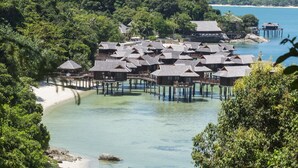 Overwater bungalows with multiple levels, connected by walkways over clear turquoise water, surrounded by lush greenery and a sandy beach. - Pangkor Laut Resort  (Pangkor Laut)