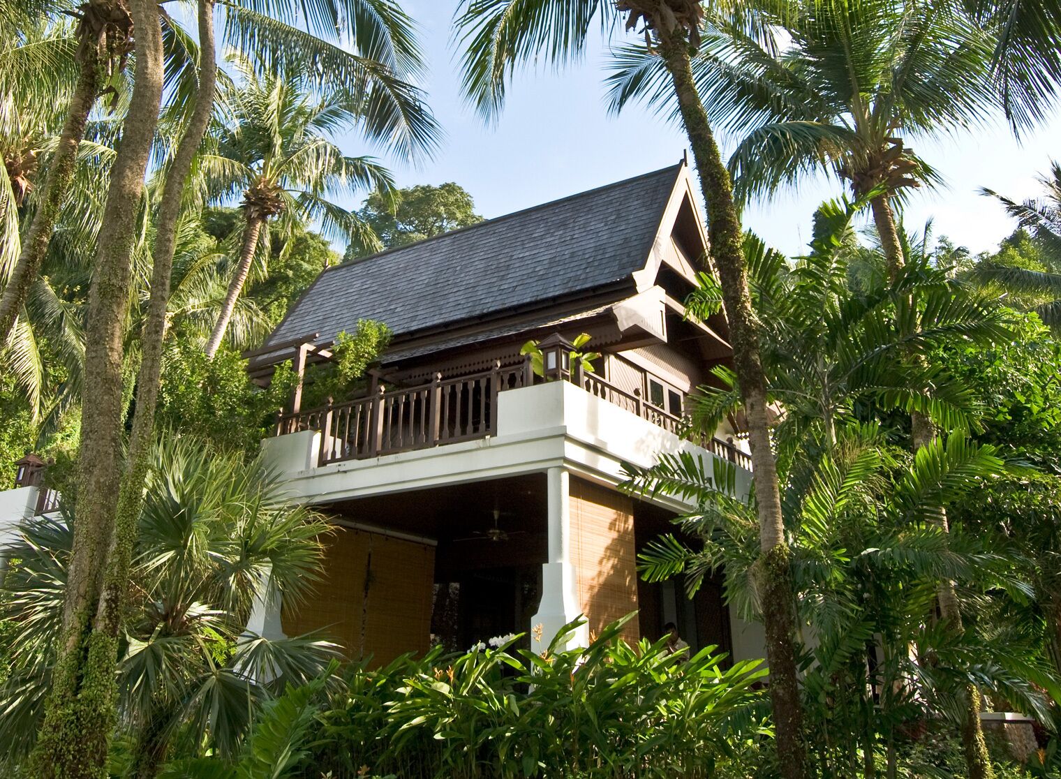 A two-story building with a balcony, surrounded by lush greenery.