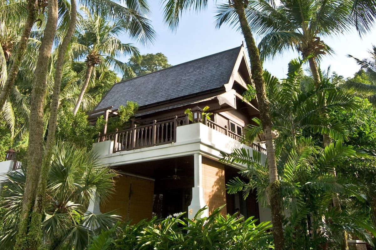 A two-story building with a balcony, surrounded by lush greenery.