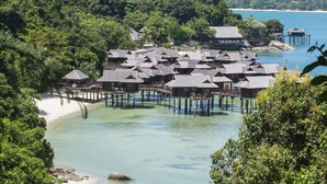 Overwater bungalows with multiple levels, connected by walkways, set against a backdrop of lush greenery and clear blue waters. - Pangkor Laut Resort  (Pangkor Laut)