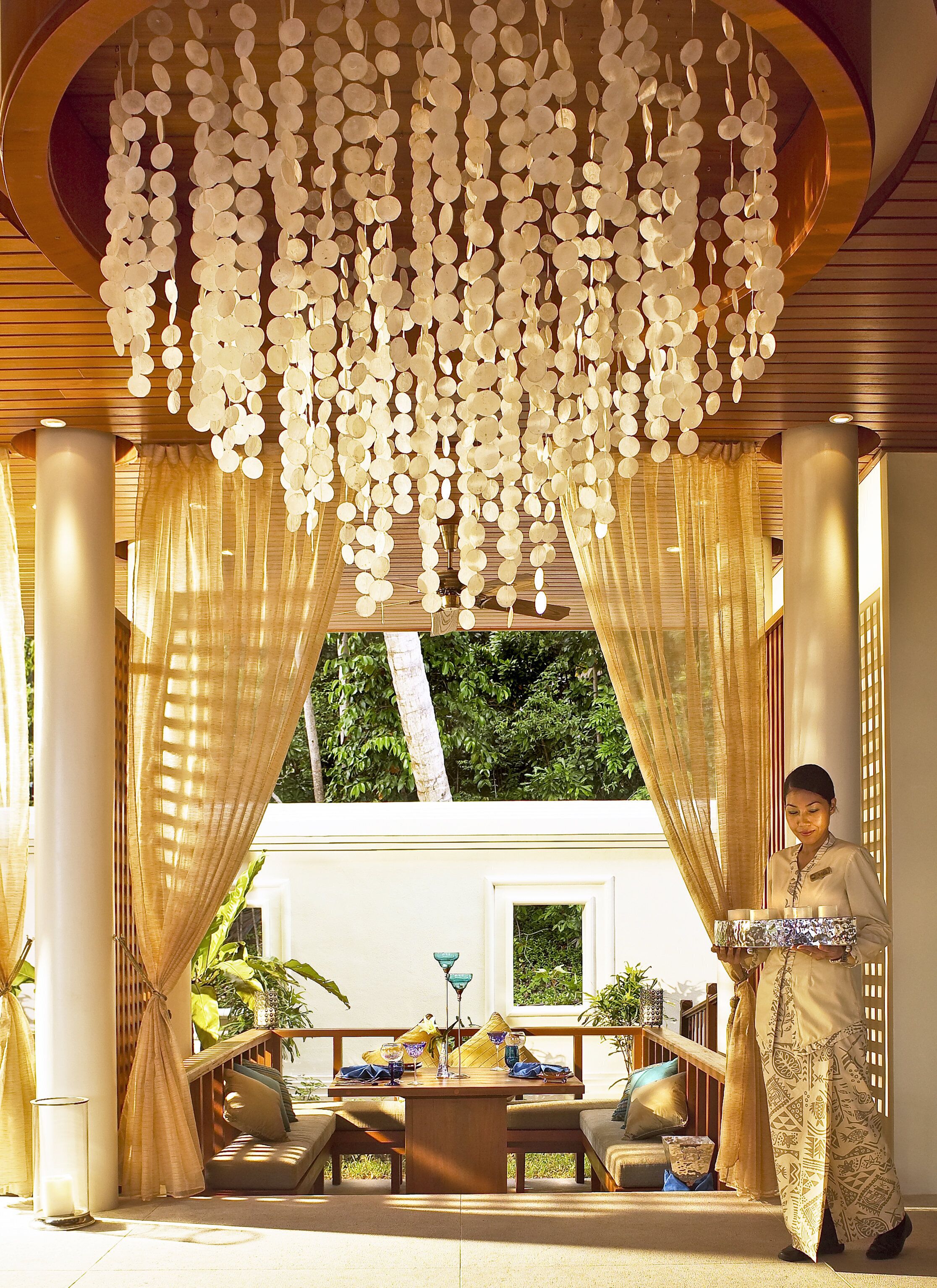 A room with a ceiling adorned with hanging circular decorations, a table set with glasses and a bowl, and a person standing by a window with curtains.