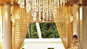 A room with a ceiling adorned with hanging circular decorations, a table set with glasses and a bowl, and a person standing by a window with curtains.