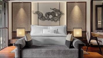 A modern hotel room with a large bed, two bedside lamps, a desk with a chair, and a decorative wall panel.