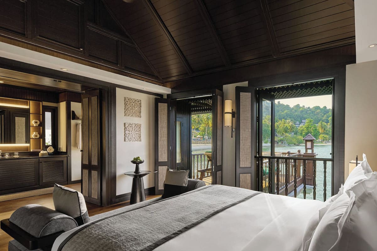 A modern hotel room with a large bed, a small table, and a balcony with a view of a lake.