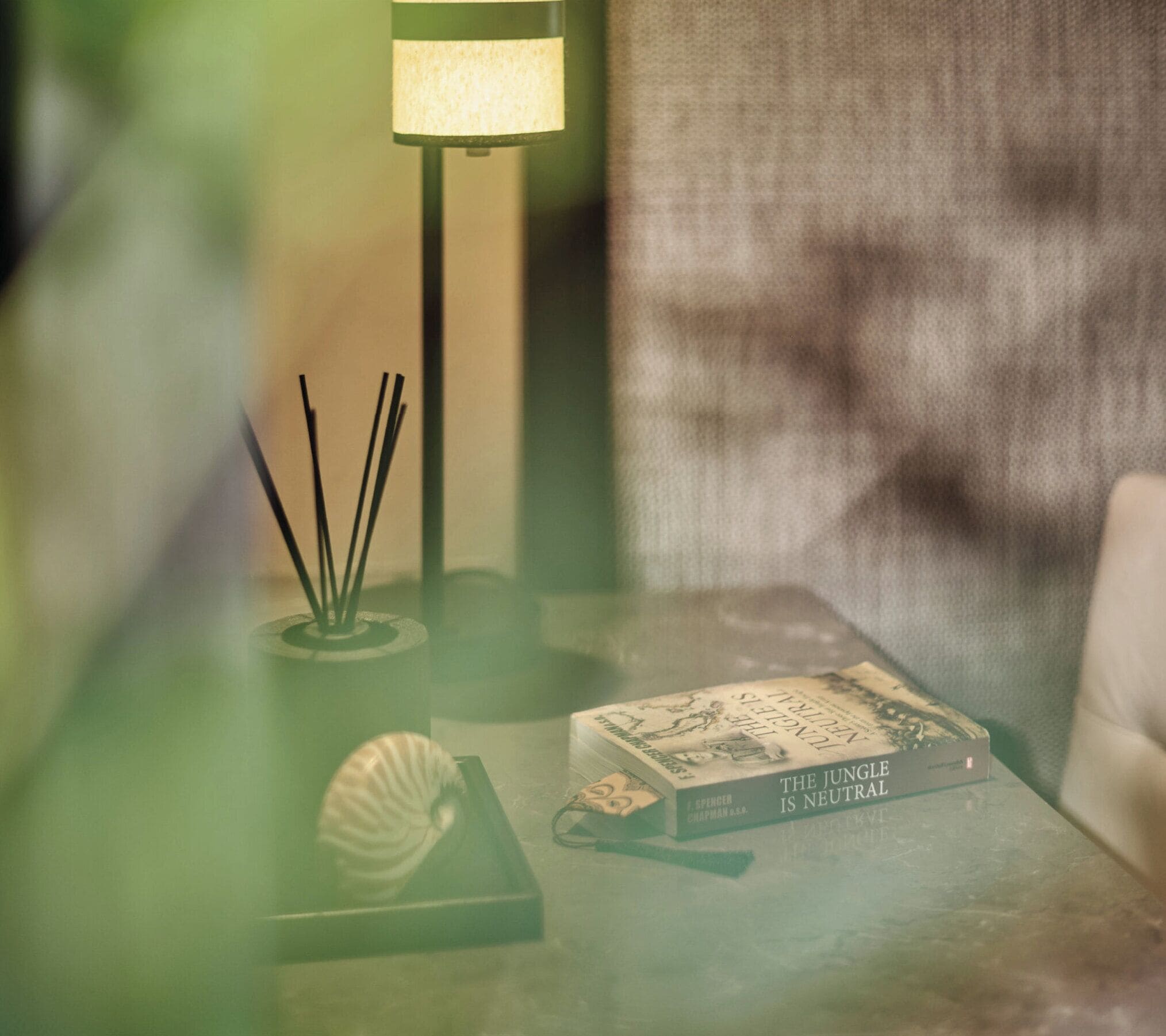 A table with a book titled 'The Jungle is Neutral' and a lamp with a green shade.