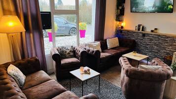 Ett mysigt vardagsrum med en soffa, fåtöljer, ett soffbord och en tv som är monterad på väggen.