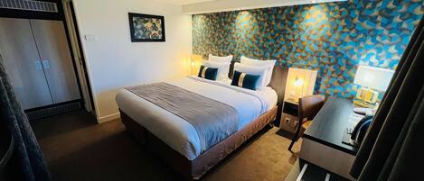 Una habitación de hotel con una cama grande, un escritorio con lámpara y un armario.