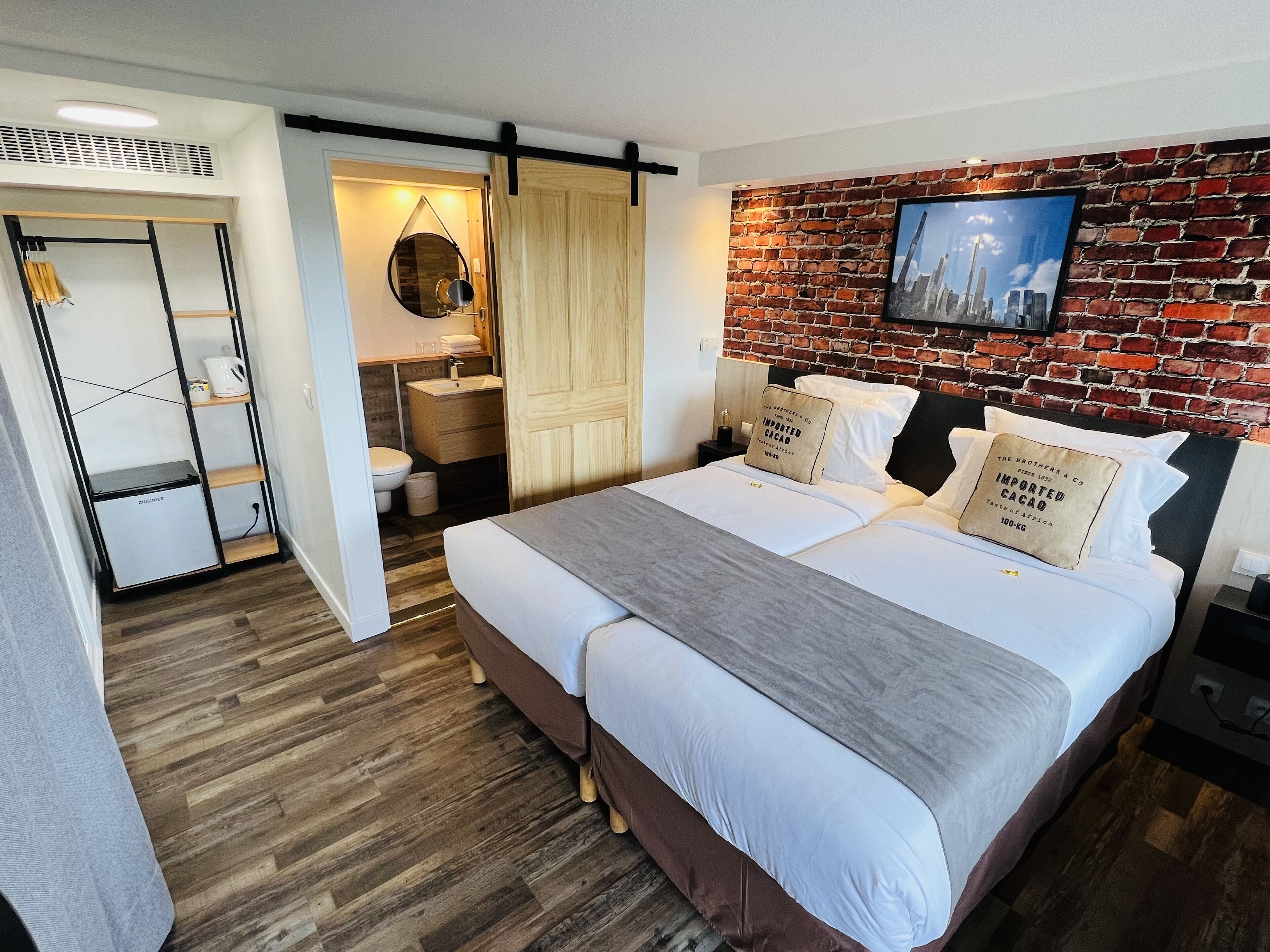 Una habitación de hotel moderna con una cama grande, un muro decorativo de ladrillo, un televisor de pantalla plana y una kitchenette.