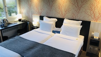 Een hotelkamer met een groot bed, een bureau met een waterkoker, een lamp en een muur met een boommotief.