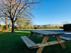 A picnic table in a grassy area with a tree and a building in the background. - Kyriad Lisieux (Lisieux)