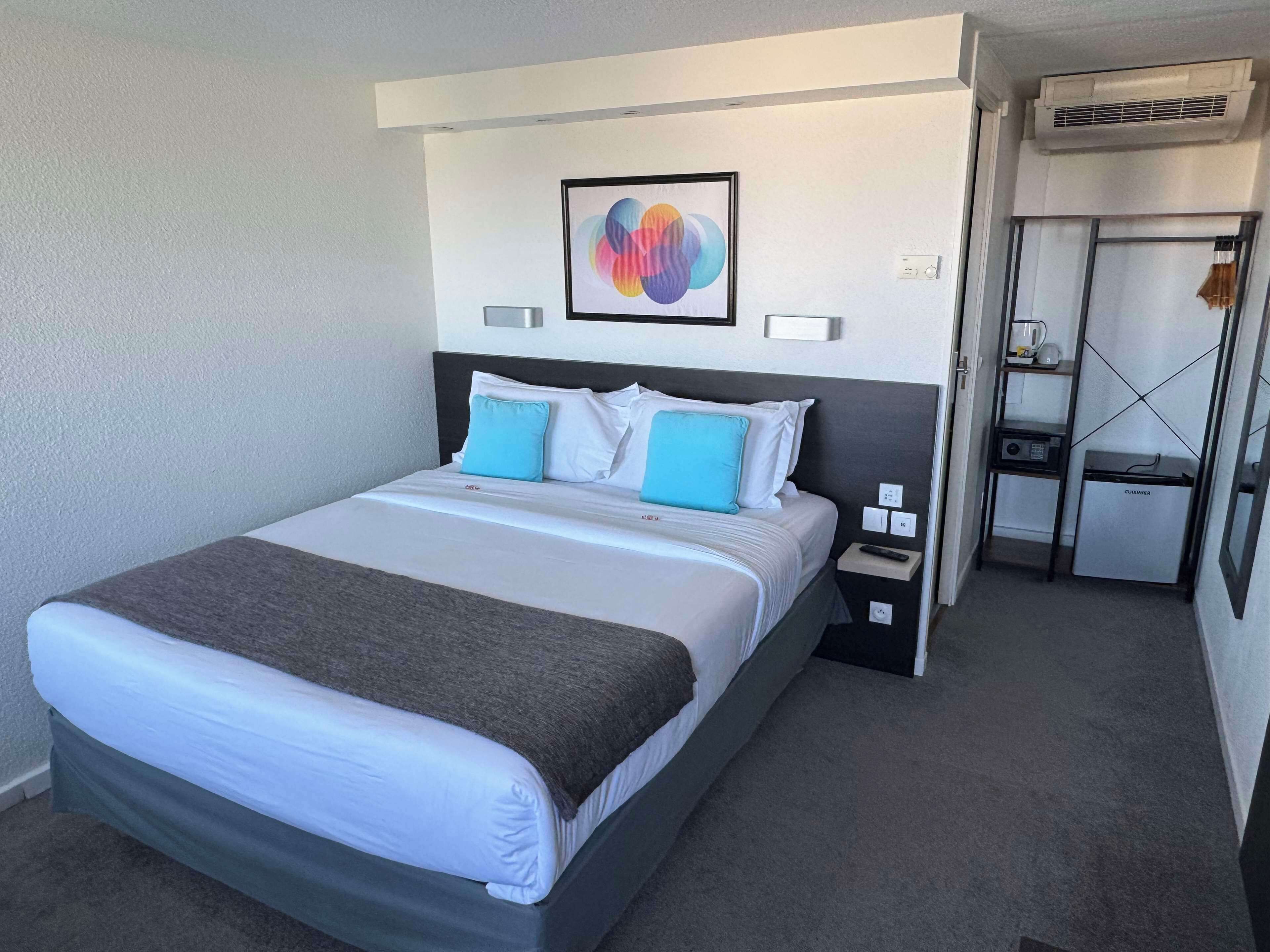 A hotel room with a bed, bedside table, and a small kitchenette.