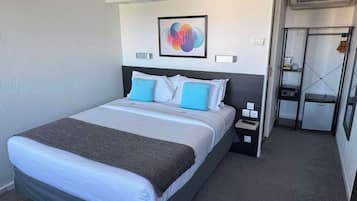 A hotel room with a bed, bedside table, and a small kitchenette.
