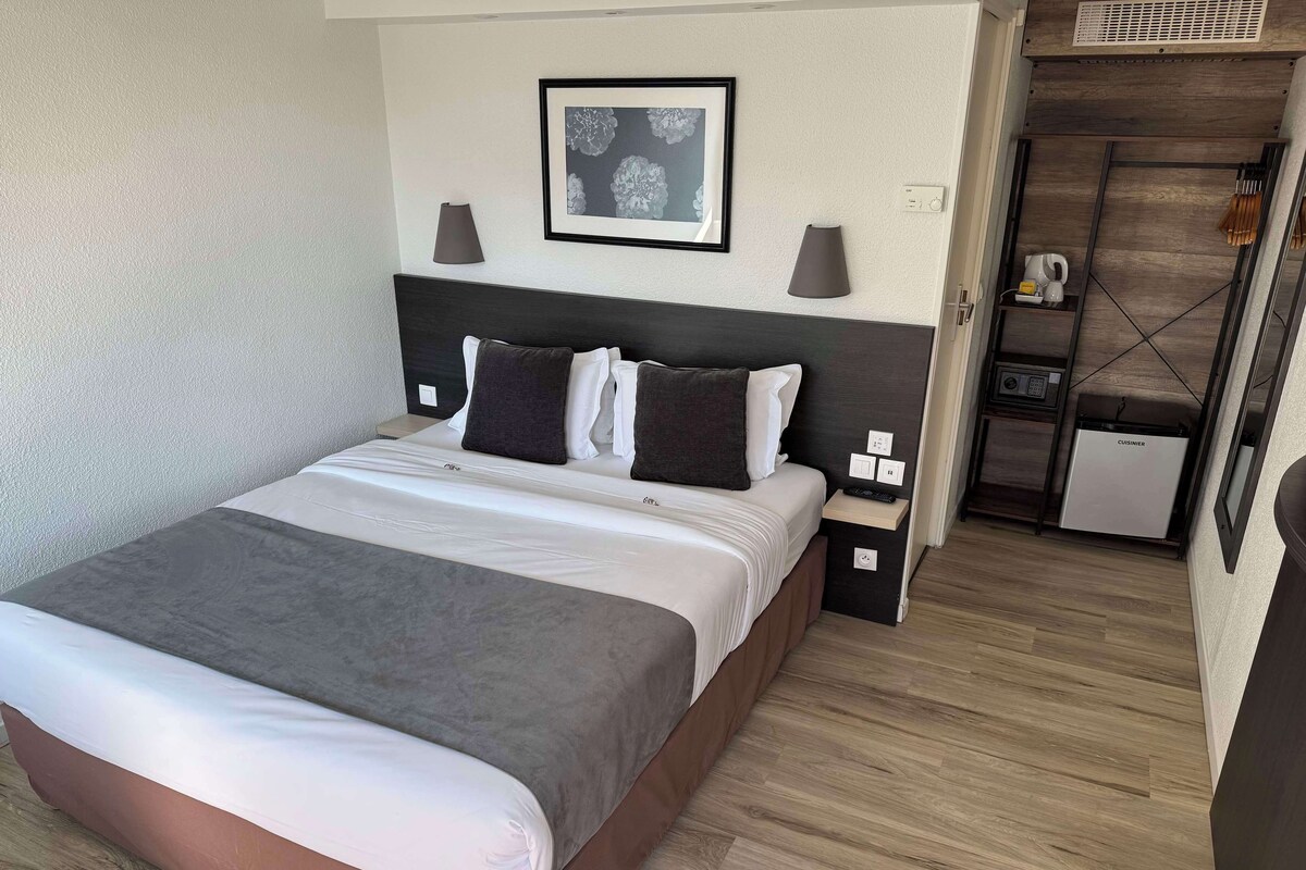 A hotel room with a bed, bedside tables, a kitchenette, and a framed picture on the wall.